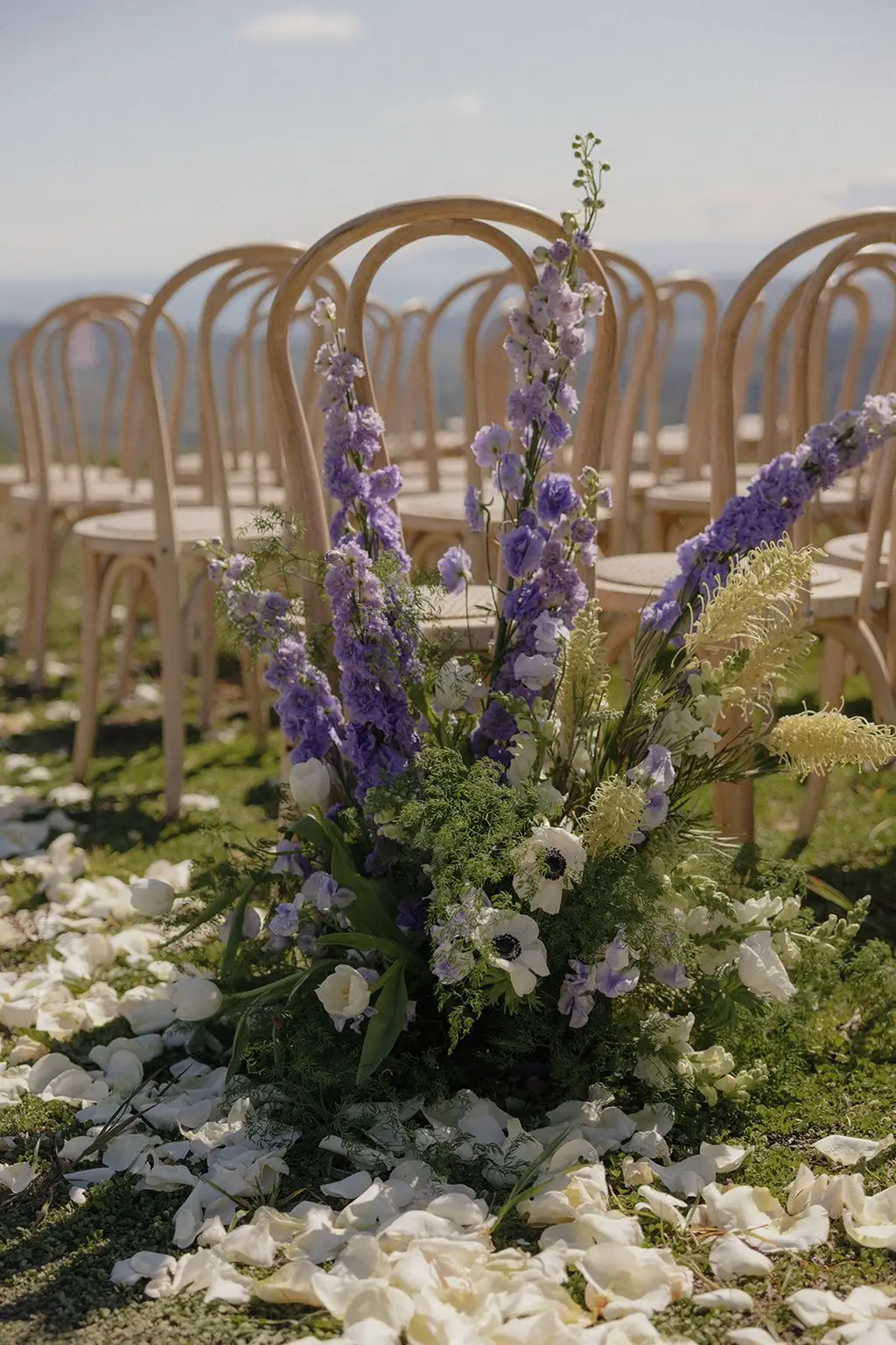 A cluster of purple delphinium and white blooms set into scattered petals at the edge of the aisle.