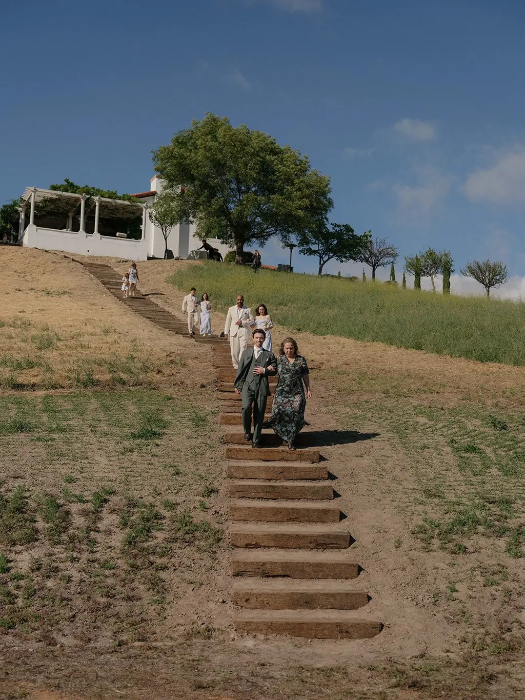 Guests walking down a long flight of railroad-tie steps cut into the hillside, the estate house on the ridge above them.