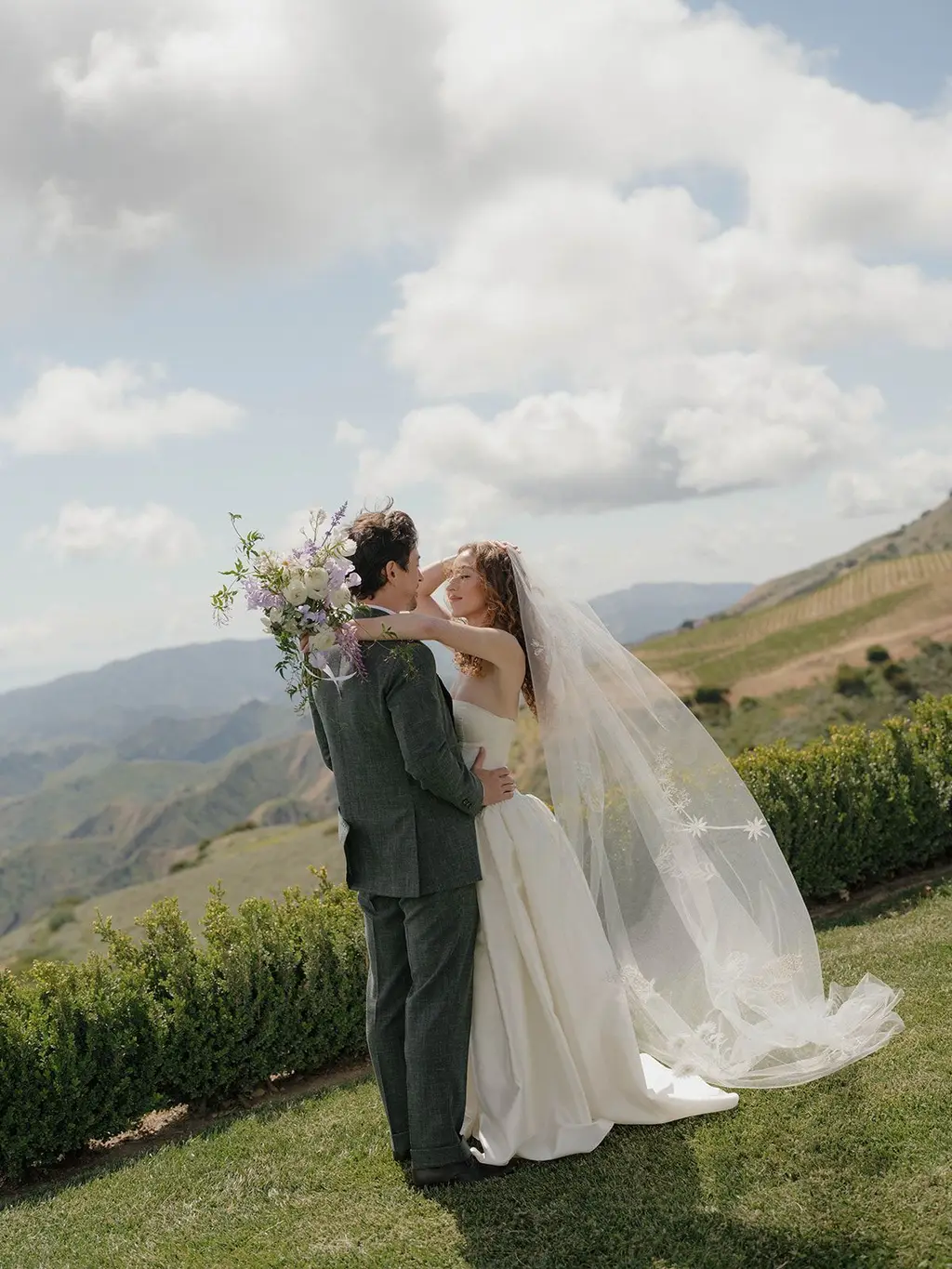 The couple on the lawn at the edge of the ridge, the bride's embroidered veil lifting in the wind.